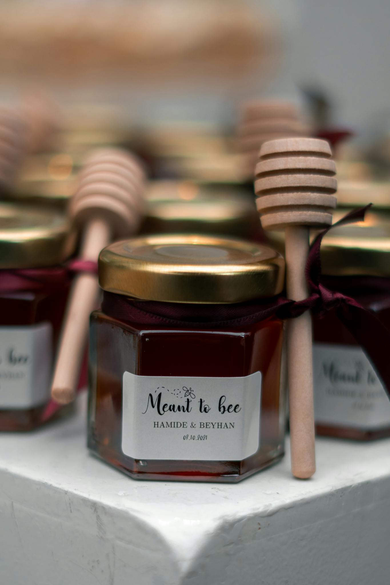 Close-up of honey jars tied with ribbons, accompanied by honey dippers, labeled 'Meant to Bee'.